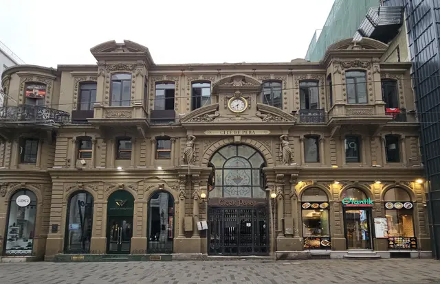 İstiklal Caddesi'nde Çiçek Pasajı'nın ön cephesi; üç katlı süslü taş yapı, ortada renkli camlı kemerli giriş, üstünde saat ve zemin katta dükkânlar.