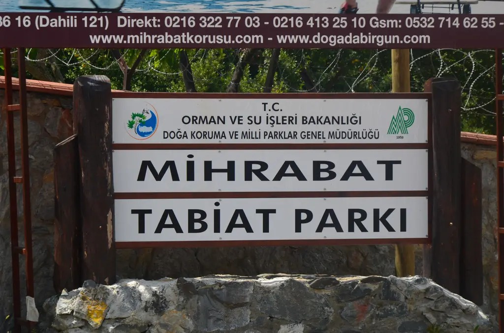 Mihrabat Tabiat Parkı'nın girişinde taş kaide üzerindeki tabela; üstte Bakanlık ve Doğa Koruma ve Milli Parklar Genel Müdürlüğü yazısı.