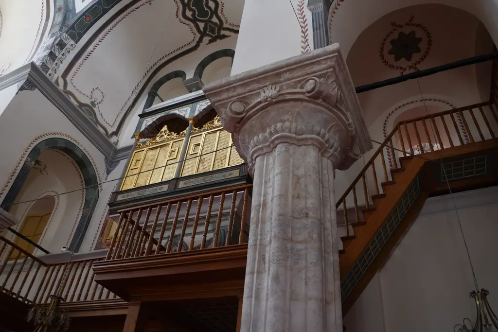 Zeyrek Camii'nde hünkâr mahfili; altın varaklı ahşap kafes bölme, yanında mermer sütun ile başlığı, arkada ahşap merdiven ve kırmızı halı.