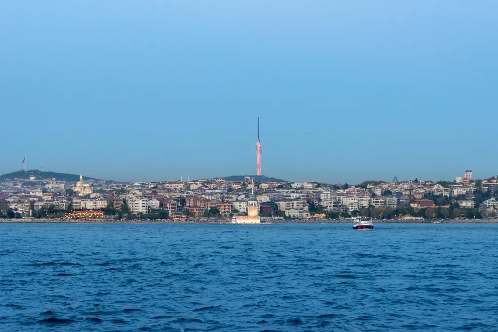 Denizden Üsküdar; kıyıda küçük Kız Kulesi, yamaçlarda sıralanan evler ve tepede ince Çamlıca Kulesi.