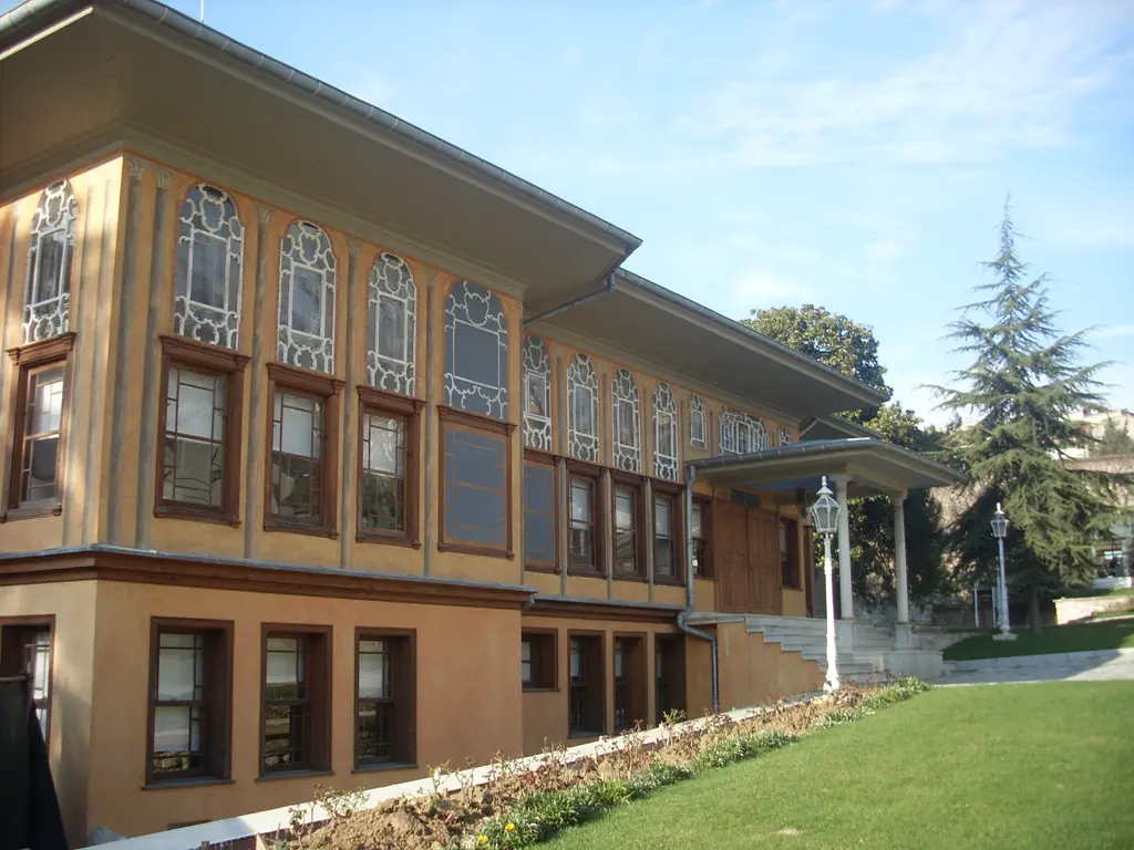 Aynalıkavak Kasrı'nın yan cephesi; uzun sarı duvar boyunca iki sıra pencere, önünde çimen ve arkada yüksek ağaçlar.