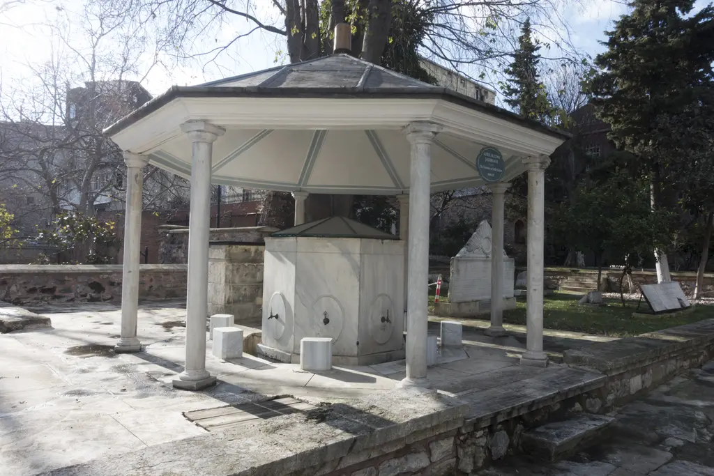 Mevlevihane bahçesinde ince sütunlu, kubbe çatılı açık şadırvan; ortasında mermer hazne ve çevresinde ağaçlar.