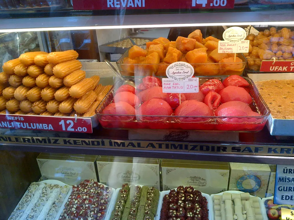 Kadıköy Çarşısı'nda tatlıcı vitrini; tulumba, ayva tatlısı, revani, altta lokum ve fiyat kartları.