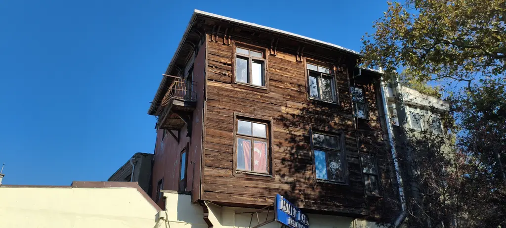 Kuzguncuk'ta kahverengi ahşap bir ev; boyasız tahta cephe, küçük balkon, dikdörtgen pencereler ve mavi gökyüzü.