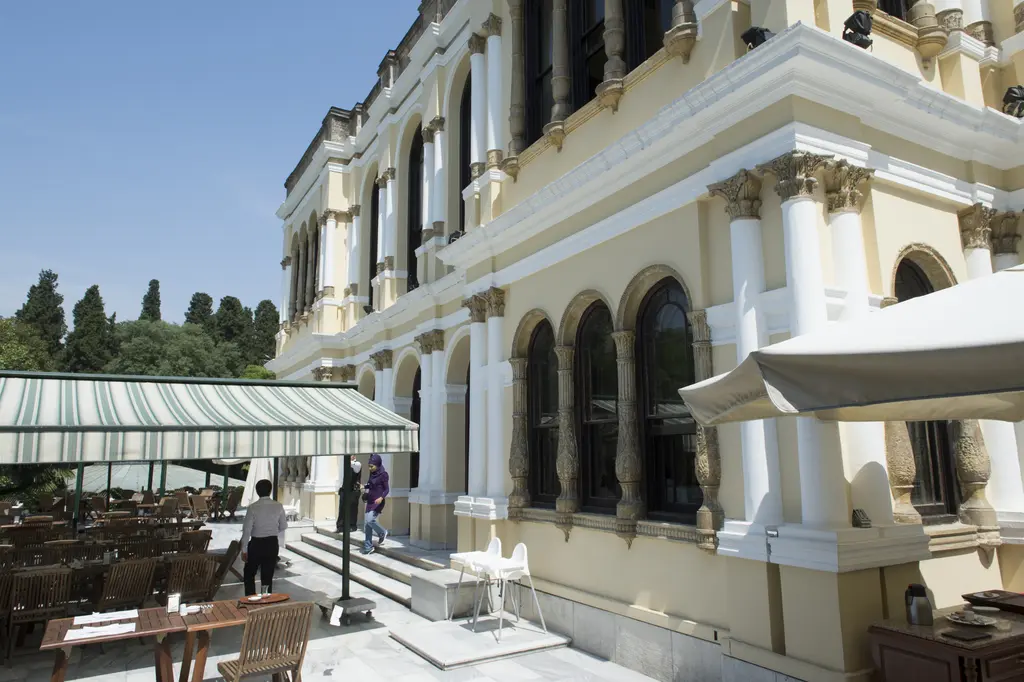 Yıldız Parkı'nda Malta Köşkü; kemerli pencereli cephe, önünde tenteli bir teras, masalar ve dolaşan ziyaretçiler.