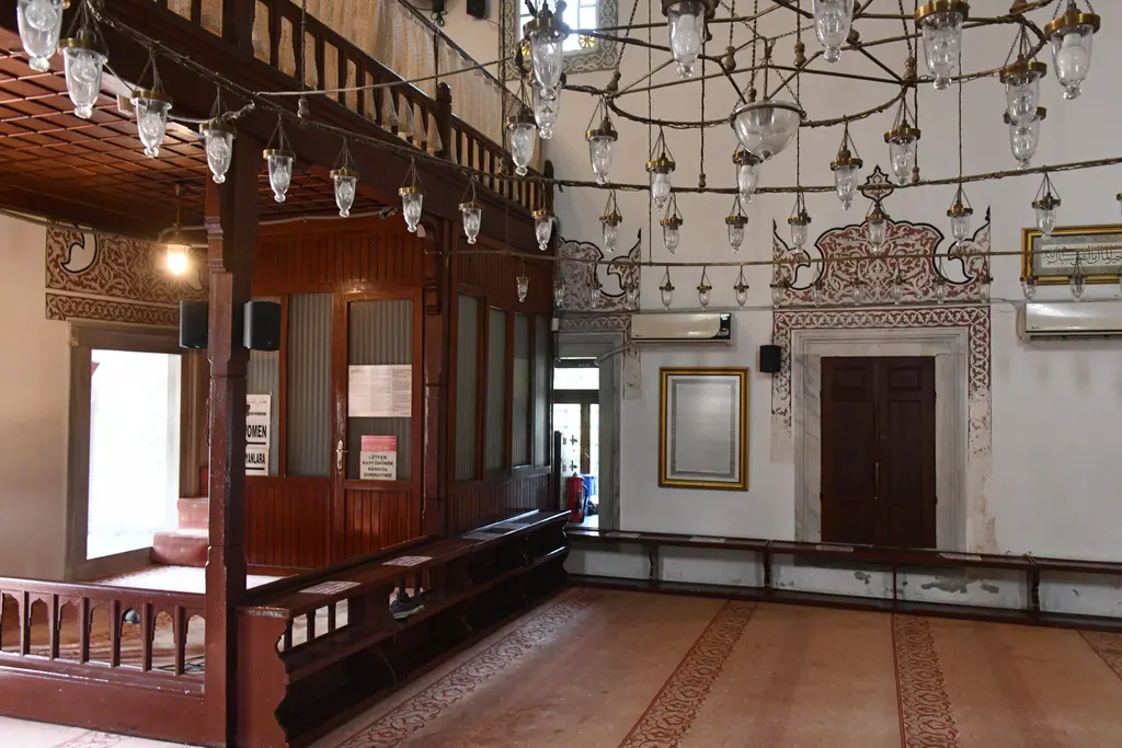 Firuz Ağa Camii'nin içinde ahşap mahfil; kırmızı boyalı korkuluklar, altında oturma yerleri, sarkan kandiller ve ahşap kapı.