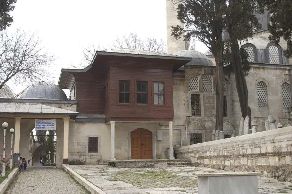 Atik Valide Camii'nde hünkâr kasrı; direkler üstünde yükselen kahverengi ahşap köşk, arkada cami.