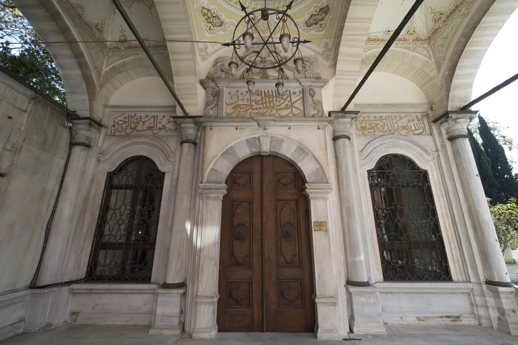 Şah Sultan Türbesi'nin kapısı; iki renkli mermer kemer, ahşap kapı kanatları, yanlarda şebekeli pencereler ve yazı kuşağı.