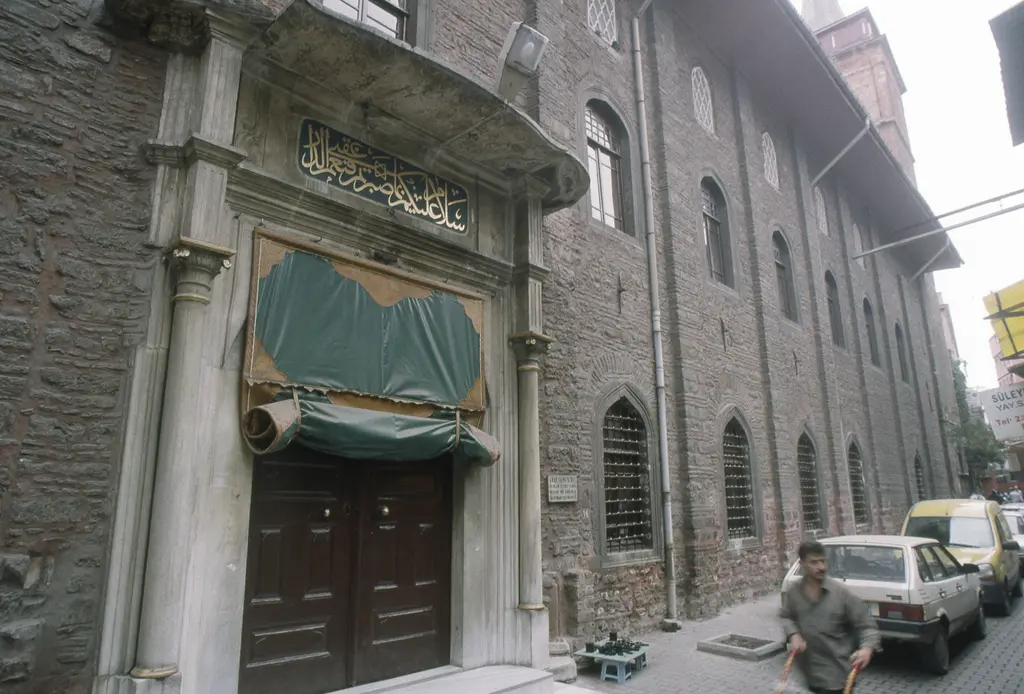 Arap Camii'nin yan kapısı; mermer çerçeveli kemerli giriş, üstünde yazı panosu, iki yanda tuğla duvar ve önde sokak.