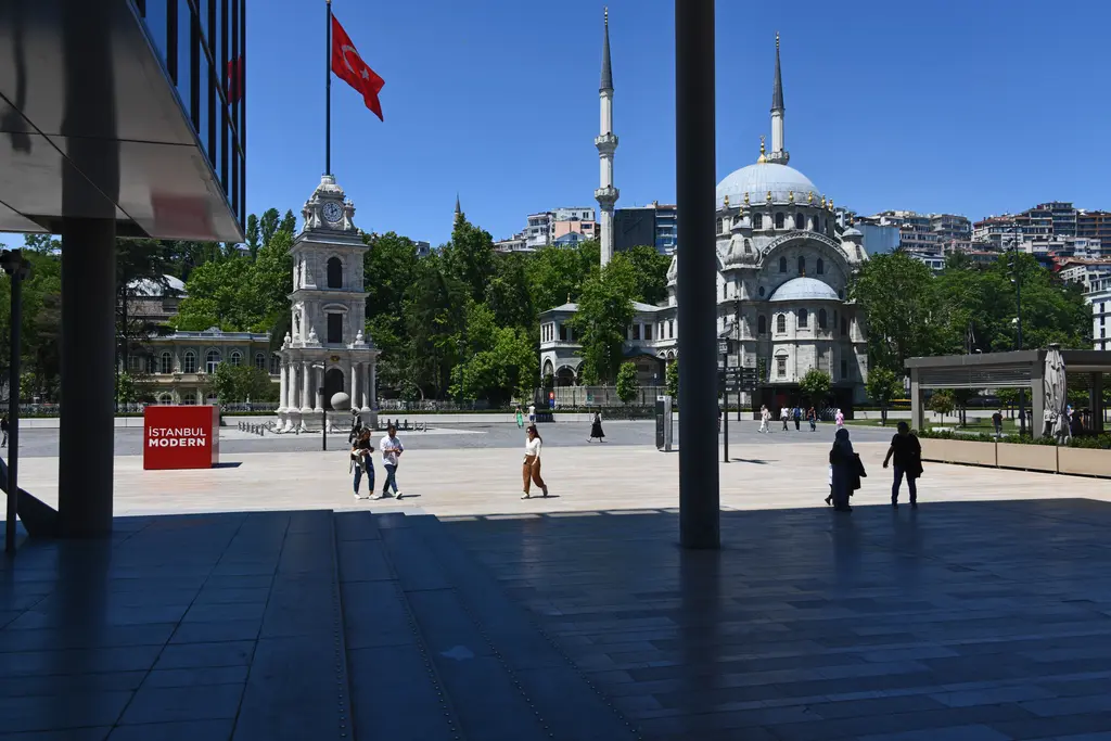İstanbul Modern'in saçağı altından meydana bakış; ileride Tophane Saat Kulesi, Nusretiye Camii ve kırmızı bir küp.