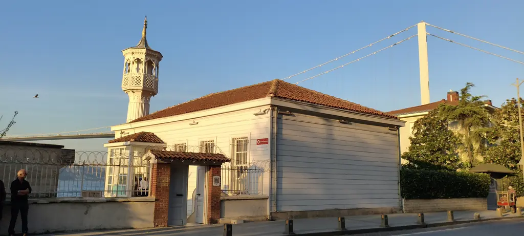 Kuzguncuk'ta Üryanizade Camii; sarı badanalı tek katlı yapı, ince minare, kiremit çatı ve arkada köprü ayağı.