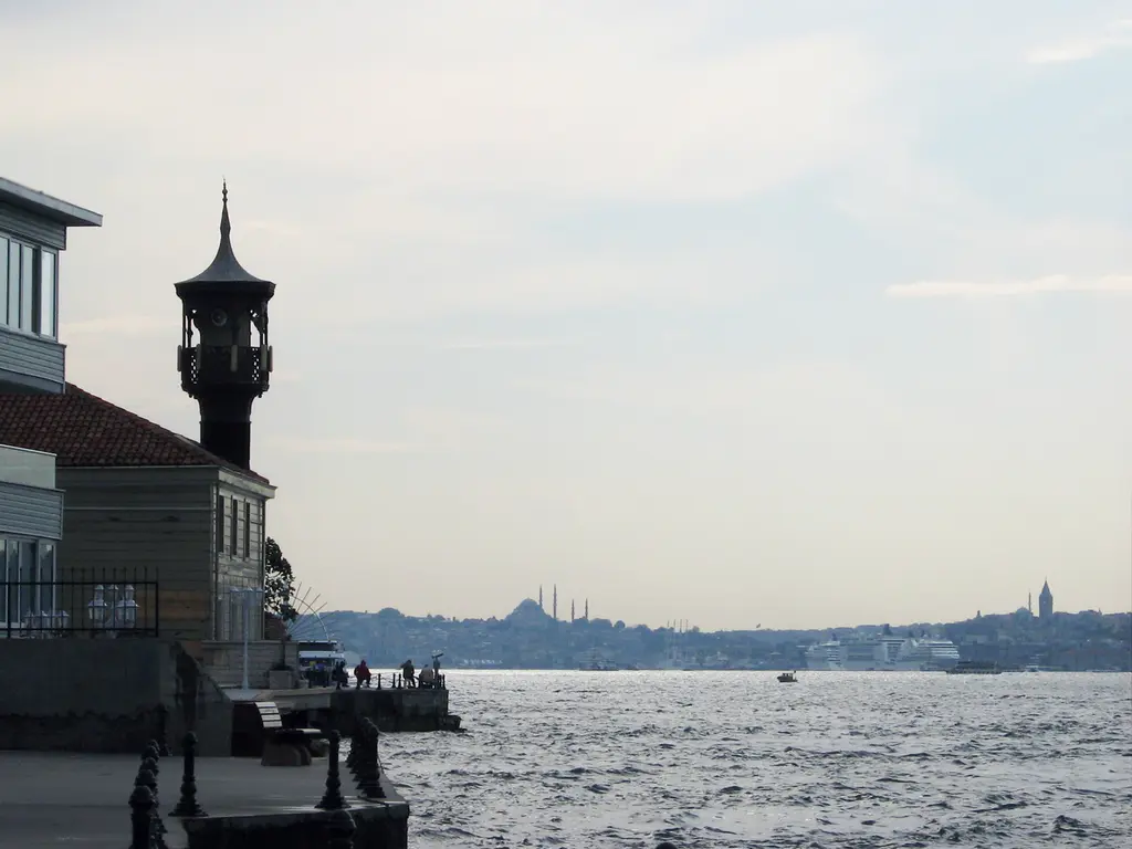 Kuzguncuk'ta Üryanizade Camii'nin minaresi; ahşap saçaklı şerefe, ince gövde ve arkada puslu Boğaz.