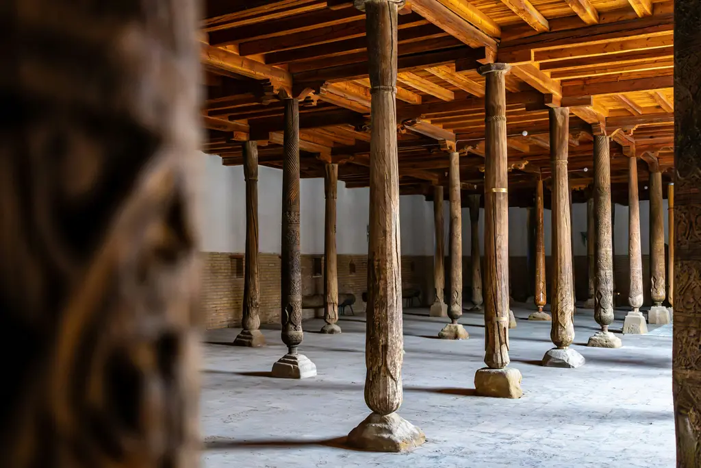 Hive'de Cuma Camii'nin iç mekânı; sıra sıra dizilmiş, üzeri oyma desenli ahşap sütunlar ve loş ışık.