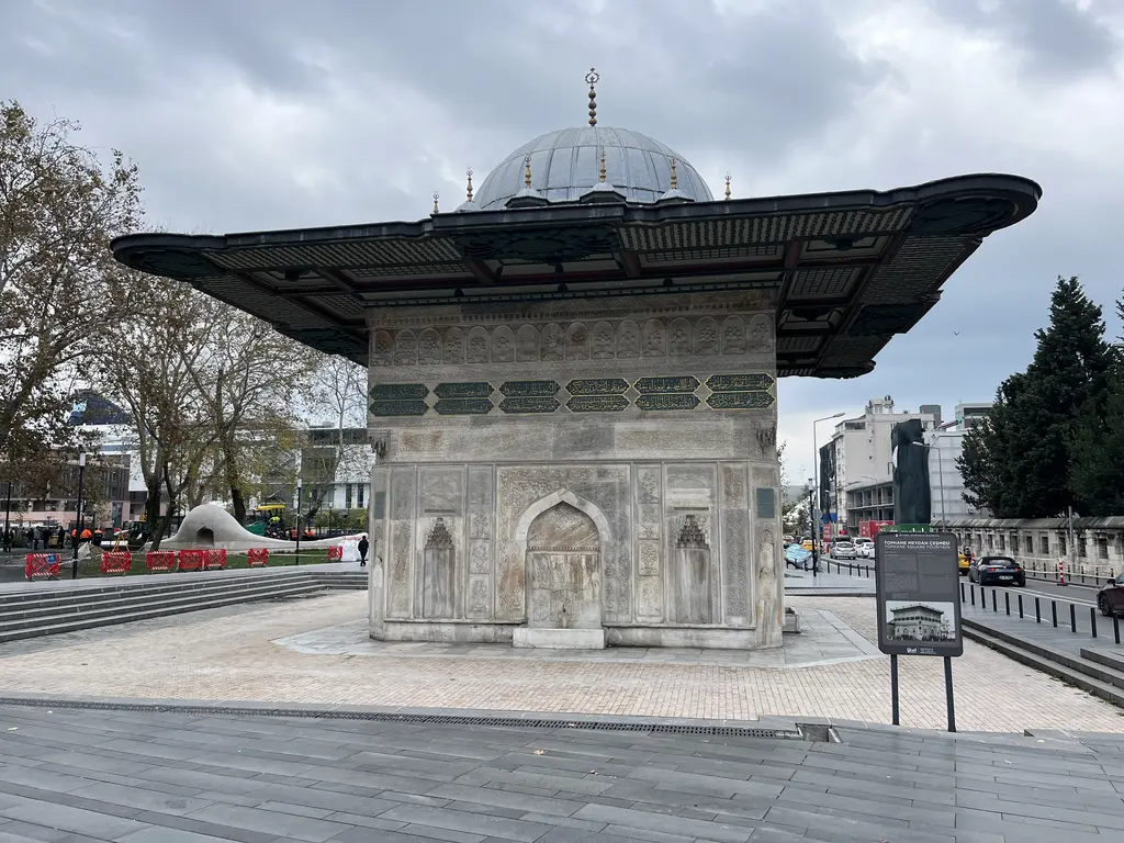 Tophane Çeşmesi'nin cephesi; ortada sivri kemerli niş, iki yanda daha küçük nişler, üstte yazı kuşağı ve geniş saçak, önde meydan.