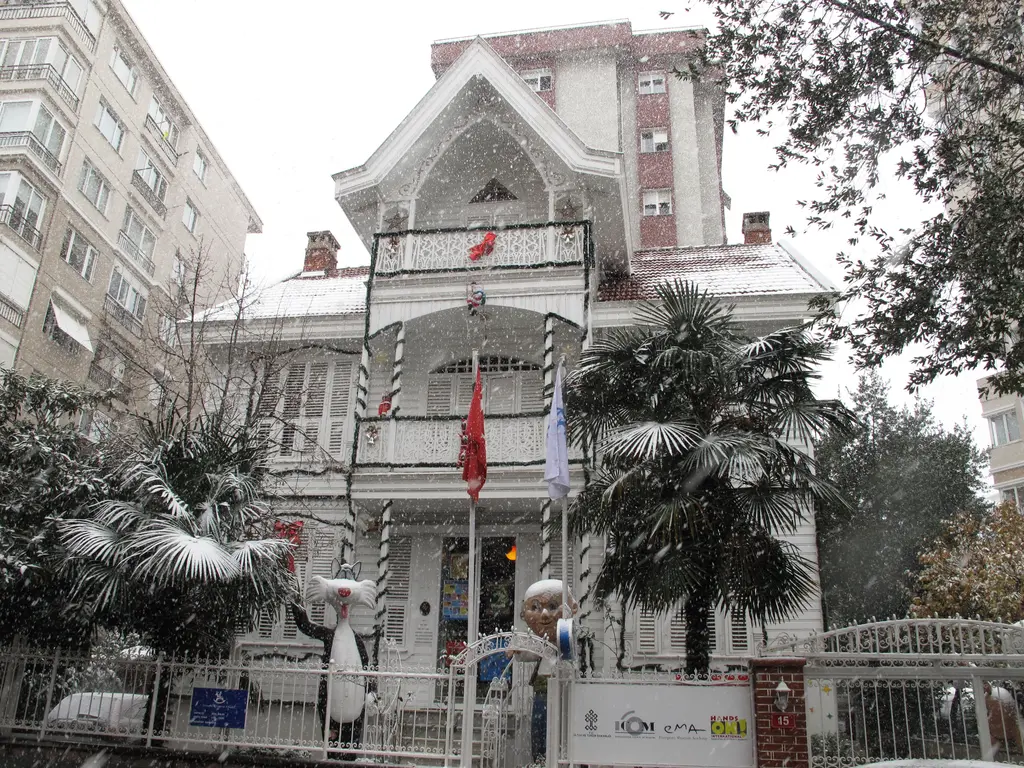 Göztepe'de İstanbul Oyuncak Müzesi; karla kaplı beyaz ahşap köşk, bahçede palmiyeler, bayraklar ve süslü kapı.