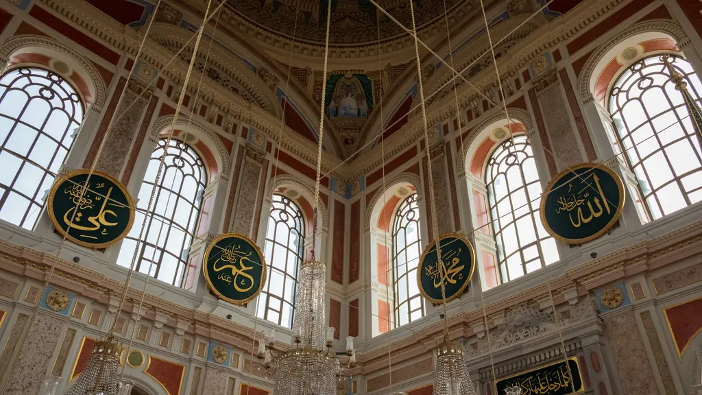 Ortaköy Camii'nin içi; büyük kemerli pencerelerden giren ışık, duvarlarda yeşil zeminli yuvarlak hat levhaları ve avize.