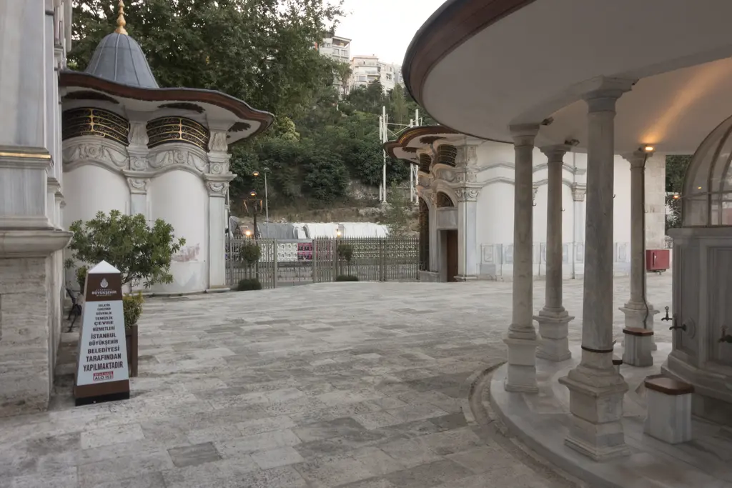 Nusretiye Camii'nin şadırvan avlusu; solda sivri külahlı muvakkithane ve sebil, ortada taş döşeli avlu, sağda şadırvanın mermer sütunları.