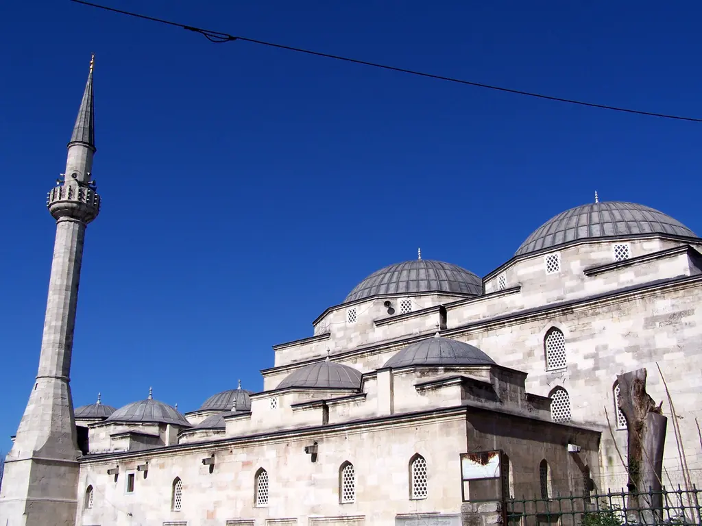Mahmut Paşa Camii'nin minaresi ve kubbeleri; çokgen gövdeli taş minare, tek şerefe, sivri külah, gri kubbeler ve koyu mavi gökyüzü.