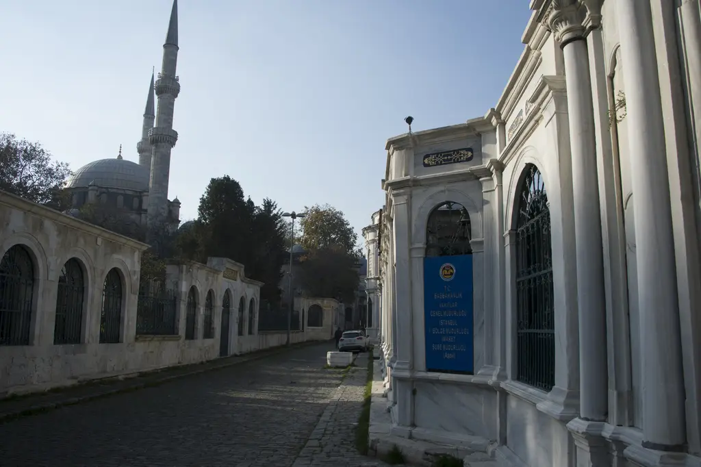 Mihrişah Valide Sultan Külliyesi önünde taş sokak; sağda mermer türbe cephesi, solda duvar ve arkada caminin minaresi.