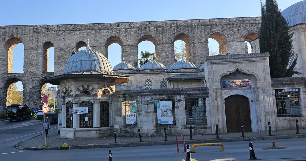 Gazanfer Ağa Medresesi cepheden; ortada kubbeli, mermer söveli sebil ile medrese kapısı, üstünde ve arkasında kemerin taş gözleri, sağda selvi ağacı ve mavi kubbeli bir yapı.