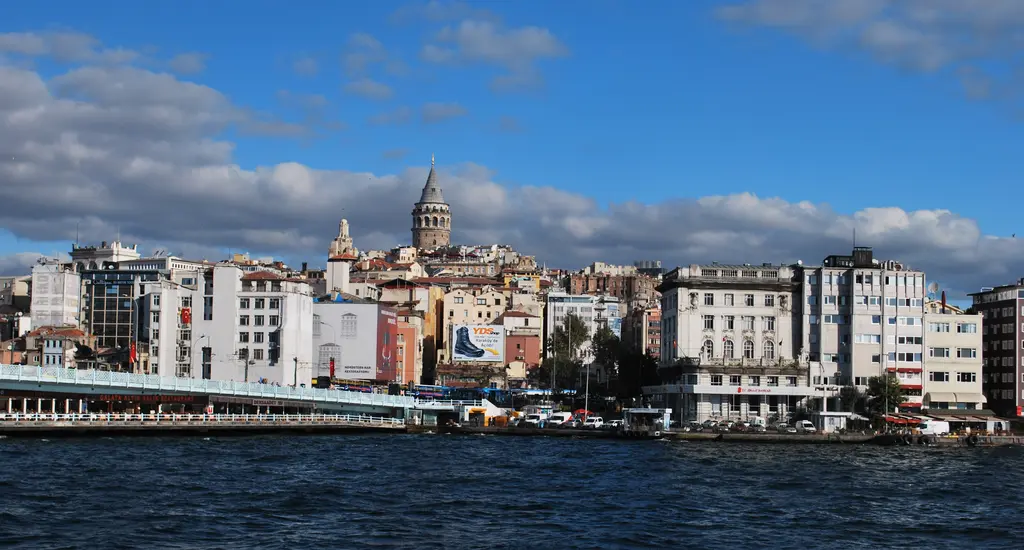 Denizden Karaköy kıyısı; beyaz ve renkli binalar, solda Galata Köprüsü'nün ucu ve yamaçta Galata Kulesi.