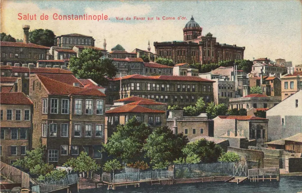 Renklendirilmiş eski kartpostal; kıyıdaki yapılar, yamaçtaki evler ve tepede okul binası, üstte kartpostal başlığı.
