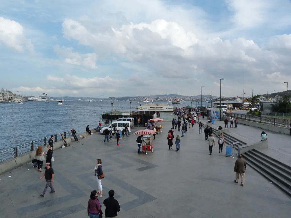 Eminönü'nde Boğaz İskelesi'ne giden kıyı yolu; geniş taş rıhtım, yürüyenler, seyyar arabalar ve uzakta Boğaz.