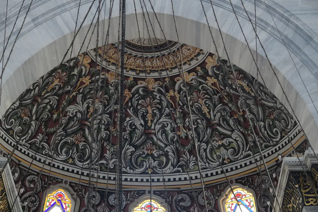 Nuruosmaniye Camii'nin mihrap apsisi; yarım kubbe içinde koyu kırmızı ve yeşil zemin üzerine yaldızlı kıvrımlı akant bezemeleri, altta renkli cam pencereler.