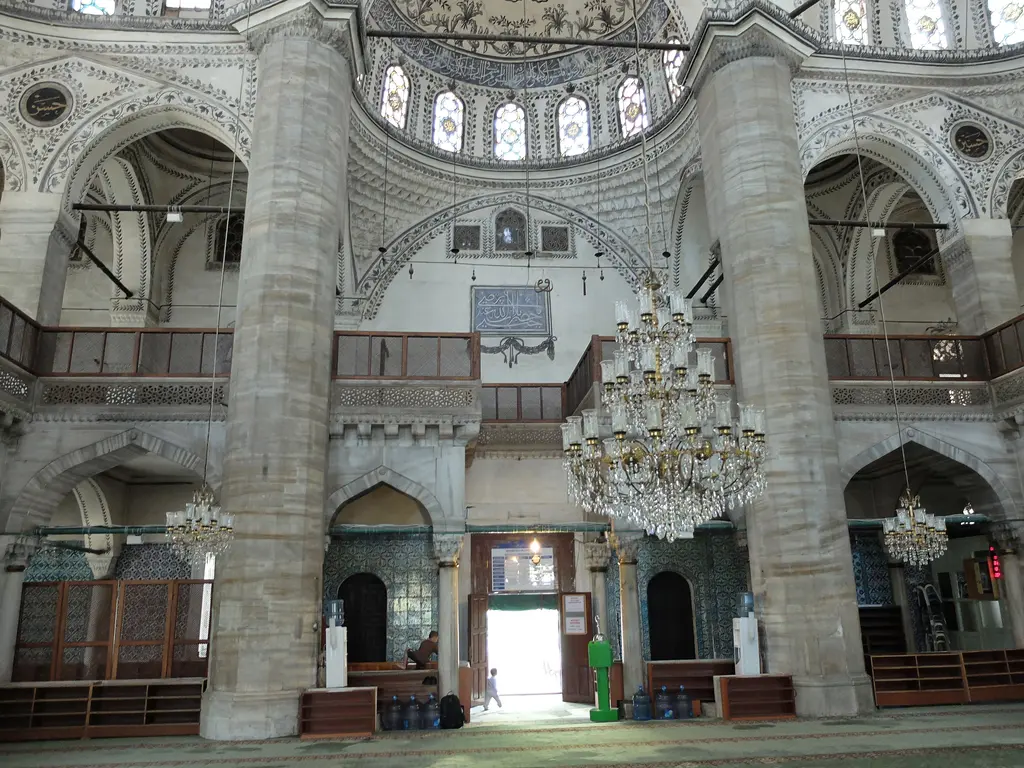 Harimde iki kalın paye arasından bakış; onikigen kesitli payeler, üstte mahfil korkulukları, ortada büyük kristal avize ve açık giriş kapısı.