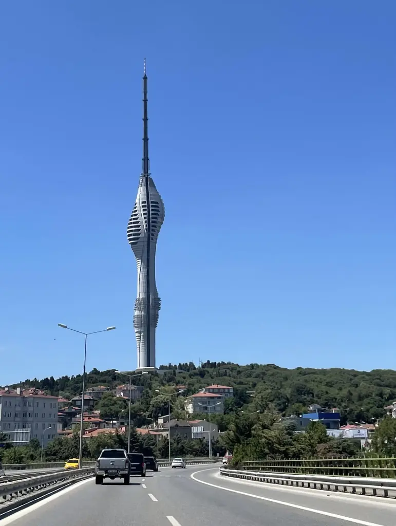 Yoldan Çamlıca Kulesi; çift şeritli yol, giden arabalar, yol kenarında ağaçlar ve tepede yükselen kule.