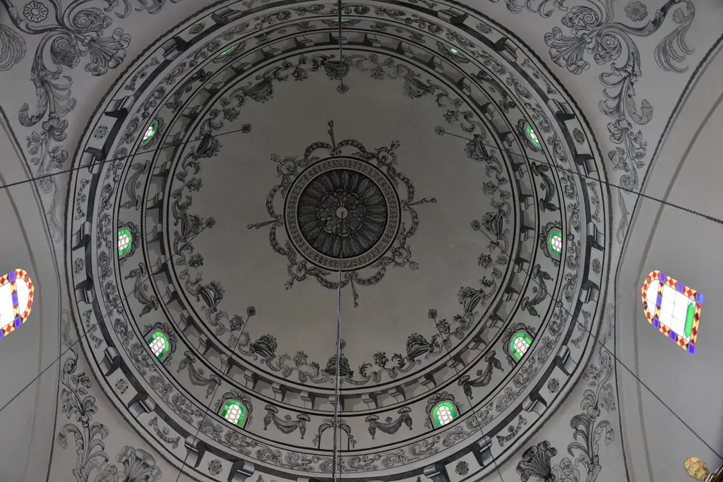 Mahmut Paşa Camii'nin kubbesi içten; ortada göbek madalyonu, siyah beyaz rumi ve bitki desenli kalem işleri, yeşil ve kırmızı camlı pencereler.