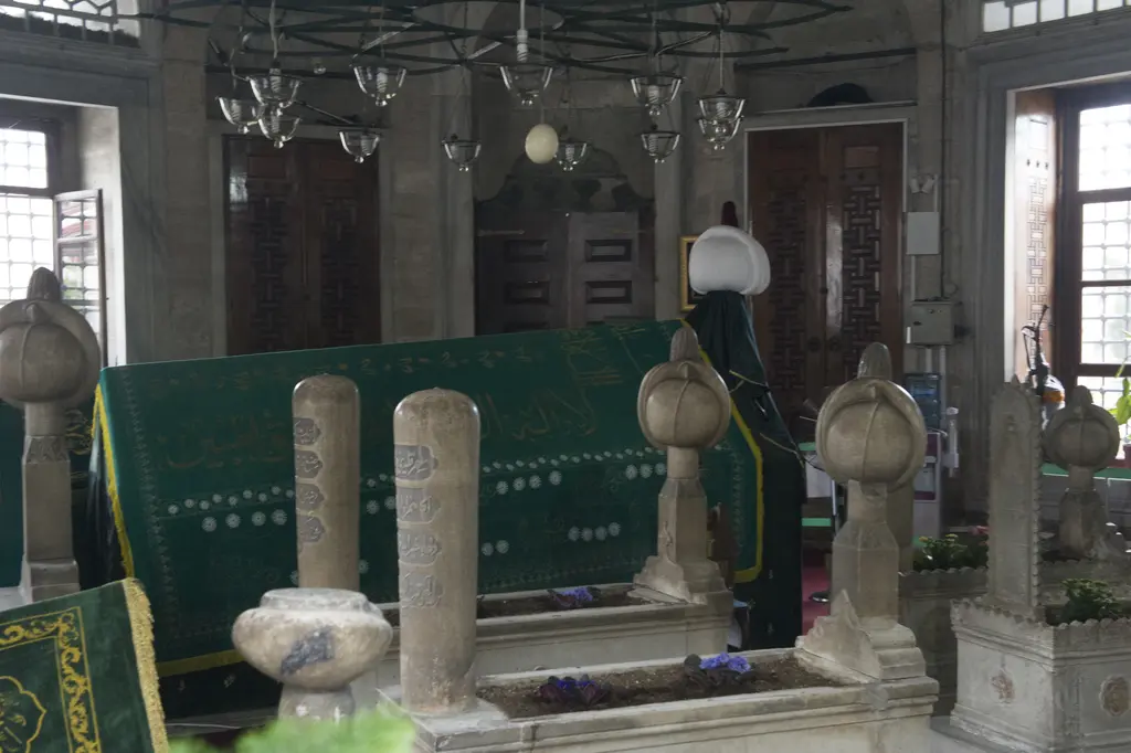 Sokullu Mehmed Paşa Türbesi'nde sandukalar; kavuklu mermer başlıklar, yeşil örtüler, kemerli pencereler ve avize halkası.