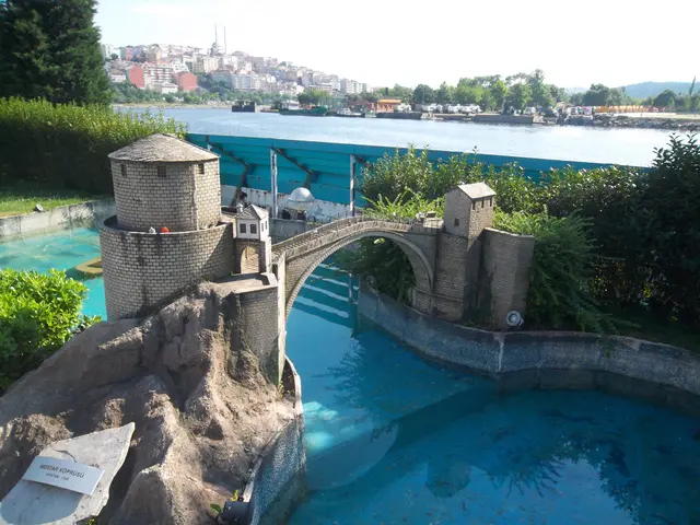 Miniatürk'te Mostar Köprüsü maketi; tek taş kemer ve iki kule, yapay kayalık üzerinde turkuaz bir dere, arkada Haliç ve karşı kıyı.