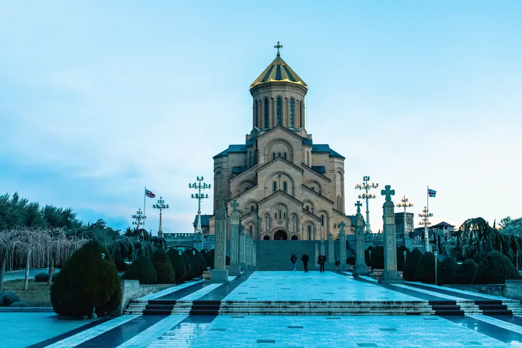 Tiflis'te Sameba (Kutsal Üçlü) Katedrali'nin altın kubbeli anıtsal yapısı; gün batımında sıcak ışıkla aydınlanan cephe.