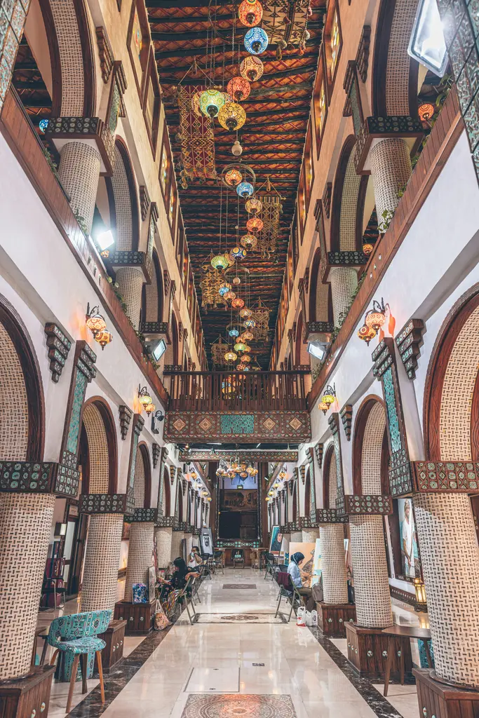 Souq Waqif'te dar bir geçit; tavandan sarkan çok sayıda metal fener, iki yanda kemerli dükkân girişleri ve loş sarı ışık.