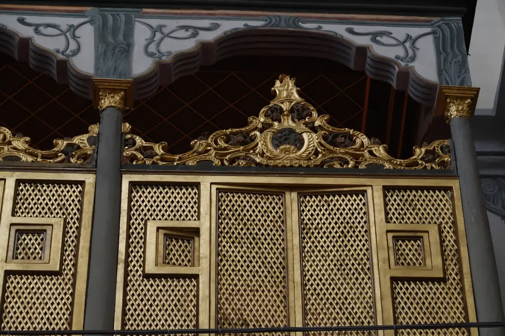 Zeyrek Camii'nde altın rengi ahşap kafes pano yakın planda; geometrik ajur deseni, üstünde kıvrımlı oymalı taç ve iki yanda yaldızlı çerçeve.