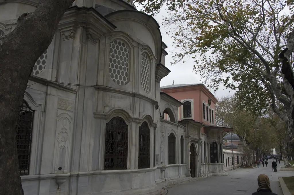 Şah Sultan Türbesi'nin yan cephesi; caddeye taşan dışbükey mermer duvar, şebekeli pencereler ve arkada ağaçlı sokak.