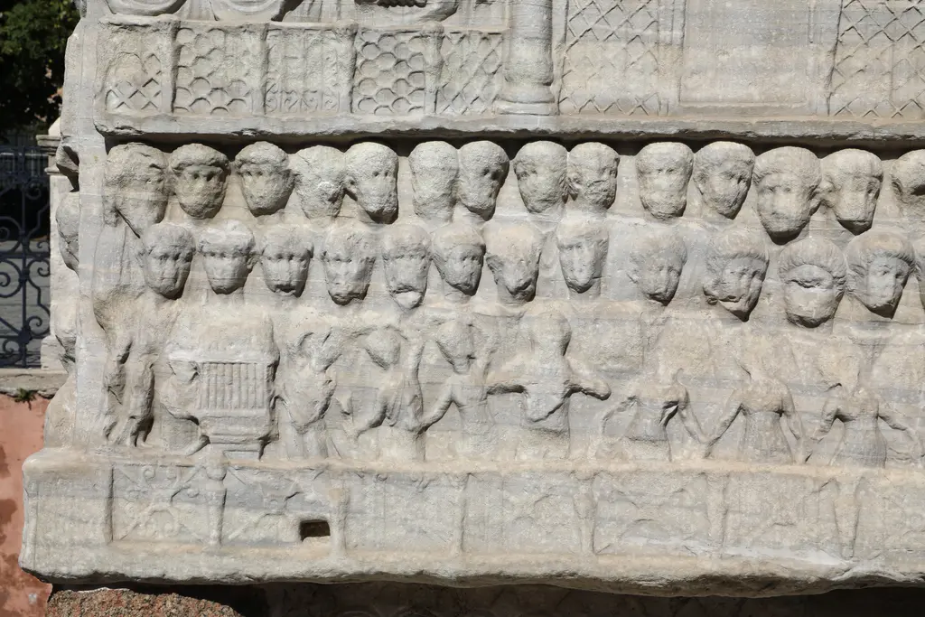 Dikilitaş kaidesinin doğu yüzünden ayrıntı; üst sırada dizili yüzler, alt sırada müzisyen ve dansçı figürleri, aşınmış mermer.
