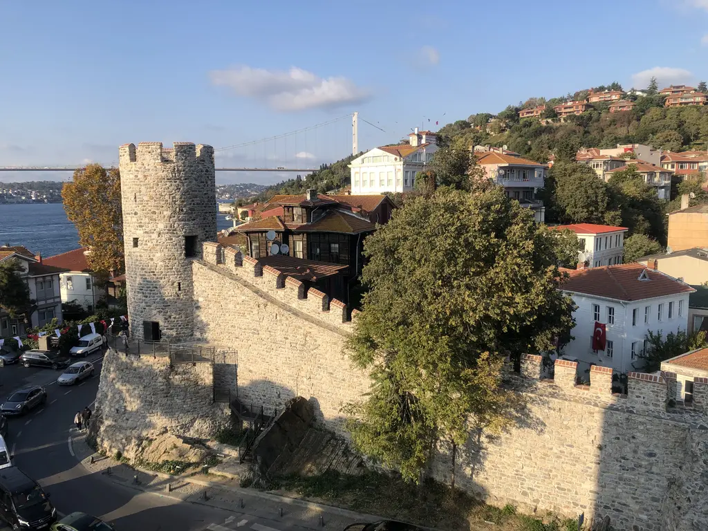 Anadolu Hisarı'nın surları yukarıdan; yuvarlak kule, mazgallı duvar, çevredeki evler ve uzakta Fatih Sultan Mehmet Köprüsü.