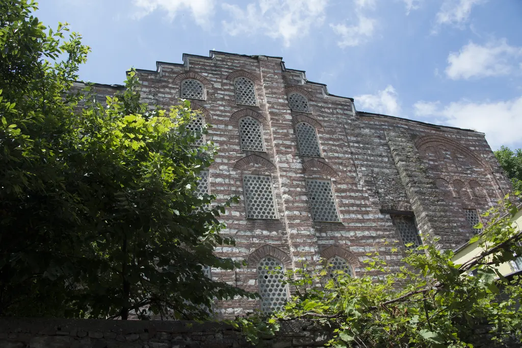 Gül Camii'nin doğu cephesi; kat kat tuğla nişler, kemerli pencereler, sarmaşıklar ve önde ağaçlar.