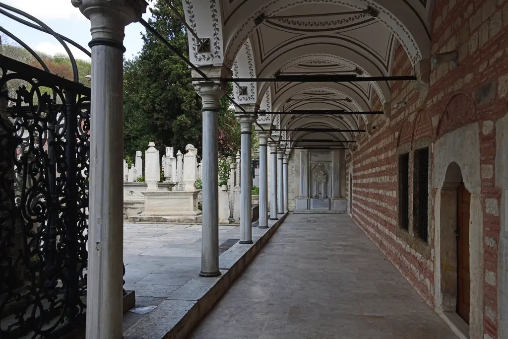Mihrişah Valide Sultan Külliyesi'nde revak; taş ve tuğla duvar, ince mermer sütunlar, kalem işli kubbecikler ve dipte bir çeşme nişi.