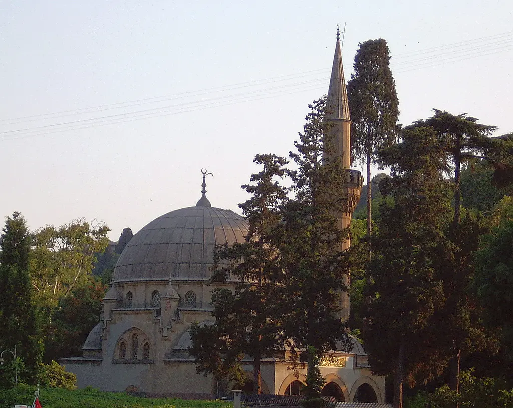 Bebek Camii; kurşun kaplı kubbe, yarım kubbeler, yüksek kaideli çokgen minare ve önünde servi ağaçları.