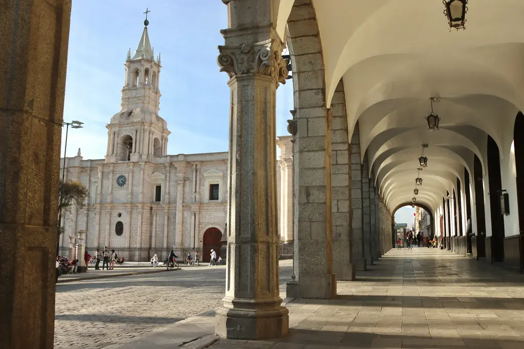 Arequipa'da Plaza de Armas; açık renk sillar taşından katedralin çan kulesi ve önünde uzanan gölgeli kemerli revaklar, taş döşeli meydan.