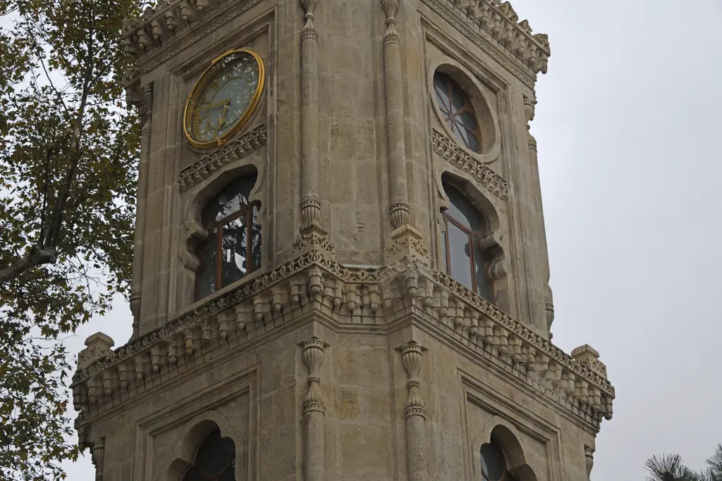 Yıldız saat kulesinin üst katları; altın çerçeveli kadran, yuvarlak gül pencereler, mukarnaslı kornişler ve sivri kemerler.