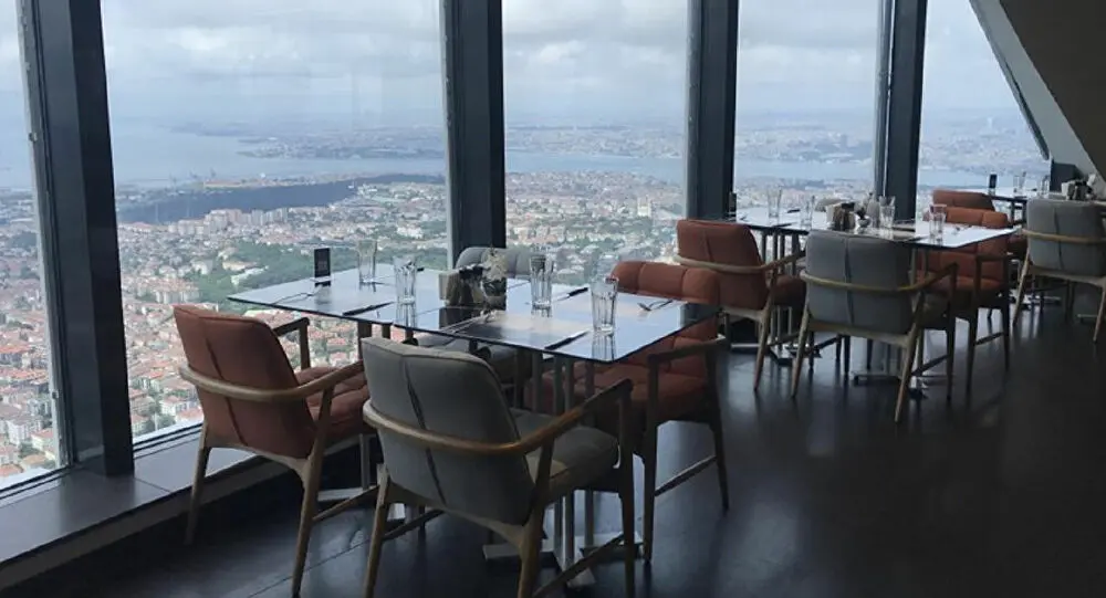 Çamlıca Kulesi'nde restoran; boydan boya camlar, deri koltuklar, kurulmuş masalar ve aşağıda şehir manzarası.