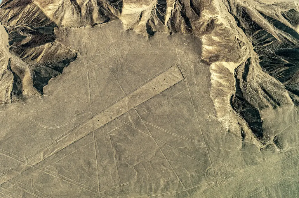 Nazca Çölü'nde geoglifler; çöl yüzeyine kazınmış dev trapez alan, kilometrelerce uzanan dümdüz hatlar ve sağdaki erozyonlu tepeler.
