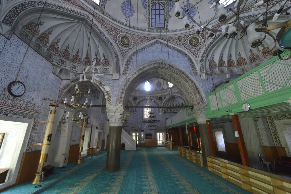 Haseki Sultan Camii'nin iç mekânı; iki sütun arasında kemerler, turkuaz halı, yeşil ahşap mahfiller, avizeler ve pencereler.