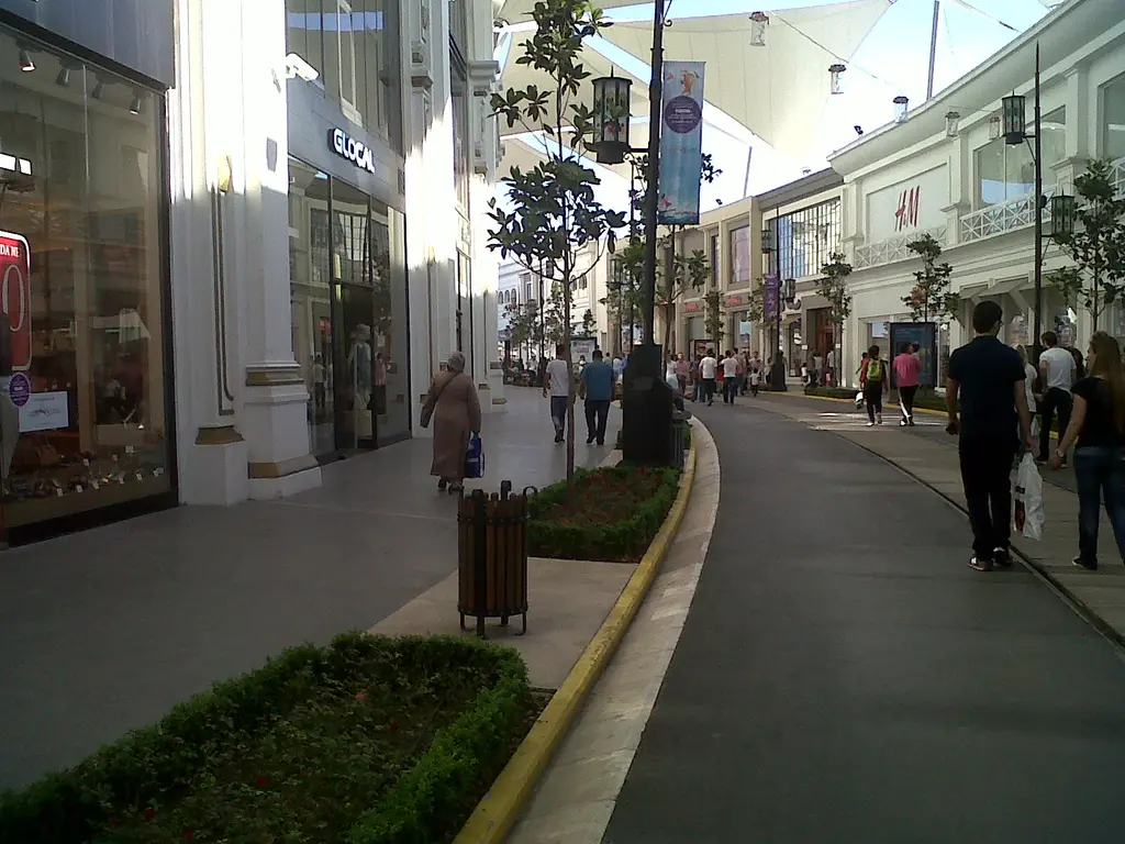 Vialand'de açık hava alışveriş caddesi; iki yanda farklı cepheli mağazalar, ortada çiçekli refüj, aydınlatma direkleri ve yürüyen insanlar.