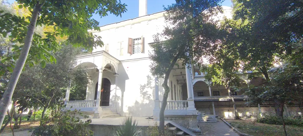 Selimiye Camii'nin hünkâr kasrı; ağaçlar arasında beyaz cephe, merdivenli giriş, kemerli balkon ve kepenkli pencereler.
