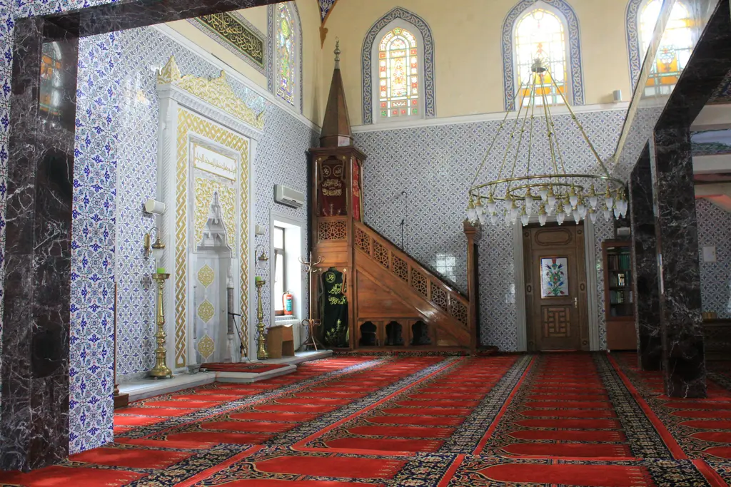 Kuzguncuk Camii'nin içi; çinili mihrap duvarı, ahşap minber, kırmızı halı ve tavandan sarkan avize.